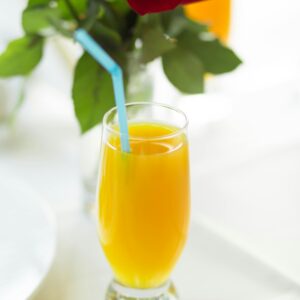 Bright orange juice in a glass with red rose bouquet, perfect for a sunny breakfast setting.