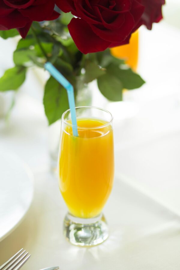 Bright orange juice in a glass with red rose bouquet, perfect for a sunny breakfast setting.